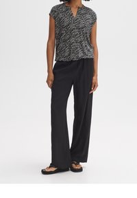 Black and white patterned short-sleeve top paired with loose black trousers. The top features a V-neck, and the fabric appears lightweight.