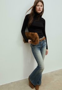 Pullover nero a collo alto, jeans a zampa d'elefante blu, cintura marrone e stivaletti. Tienendo una pochette in pelliccia sintetica marrone. Tessuto liscio e design attillato.