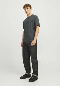 Pelēks kokvilnas T-krekls ar iekšējo tekstu krūšu rajonā, apvienots ar tumšiem džinsu biksēm un melniem apaviem ar šņorēm un reljefa zoli.