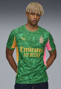 Vihreä urheilupaita, jossa on teksturoitu viidakon kuvio, keltaisen ja vaaleanpunaisen korostuksin. Suunnittelussa on Puma-logo ja "Emirates Fly Better" -teksti.