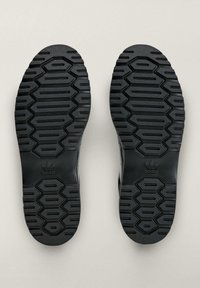 Crni gumeni đonovi cipela s teksturiranim uzorcima, s heksagonalnim i pravokutnim oblicima za prianjanje, s logotipom adidas brenda.