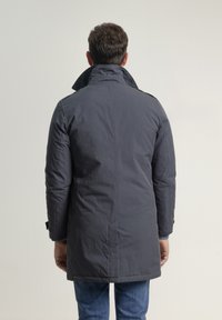 Abrigo gris aislante con cuello alto, tela texturizada, bolsillos laterales y puños con botones, que llega hasta la mitad del muslo.