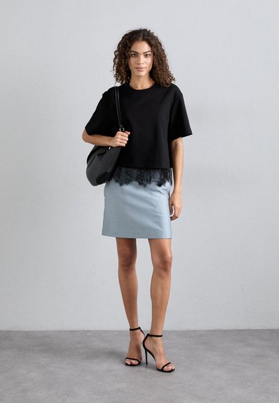 Μαύρο κοντό μπλουζάκι με δαντελένια περίποιηση, ανοιχτό μπλε φούστα και μαύρες ψηλοτάκουνες σανδάλια. Κουβαλάει μια μαύρη τσάντα χεριού. Λείες υφές.