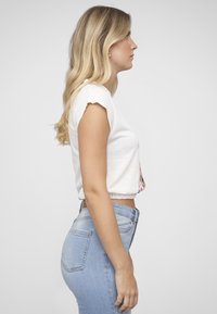 Hvit kort t-skjorte med korte ermer, med et fargerikt grafisk design på forsiden. Sammen med blå jeans med middels høy midje.