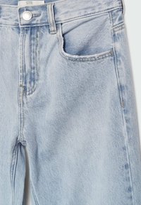 Vaqueros de mezclilla azul claro con una cintura alta, diseño de cinco bolsillos y un ligero desvanecimiento. Costura clásica y detalle de botón de metal en la cintura.