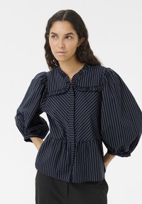 Marine gestreiftes Blusenshirt mit Rüschensaum, puffigen Ärmeln und einem Peplum-Taille. Der Stoff hat eine glatte Textur mit vertikalen weißen Streifen.