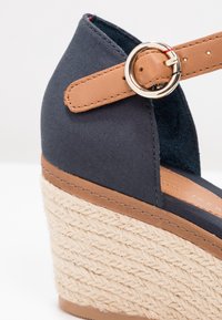 Sandale compensée en tissu marine avec talon espadrille tissé, bride de cheville en cuir tan et fermeture à boucle ronde dorée.