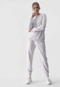 Helles graues Sweatshirt und passende Jogginghosen, mit weicher Textur und gerippten Bündchen, kombiniert mit weißen Sneakers, vor einem einfarbigen Hintergrund.