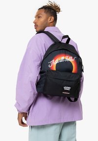 Sac à dos en tissu noir avec un design arrondi, arborant un dégradé de couleurs arc-en-ciel et le texte "C'est tout, mes amis !" à l'arrière, marqué des logos Looney Tunes et Eastpak.