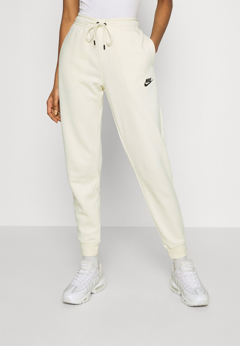 Joggers creme com um cós elástico, apresentando um logo preto da Nike. O tecido parece liso e suave, com punhos ajustados nos tornozelos.