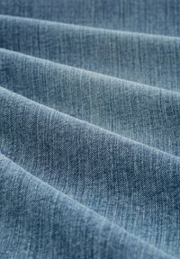 Tela de mezclilla azul con una textura suave, que muestra múltiples capas dobladas. Presenta patrones de tejido sutiles y un degradado de color uniforme.