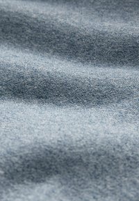 Tessuto denim di un azzurro chiaro, caratterizzato da una consistenza liscia e un sottile motivo di trama. Il materiale presenta pieghe e scolorimenti delicati.