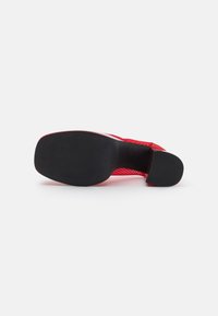 Zapato rojo con un upper texturizado y detalles de malla, una suela negra lisa y un tacón redondeado para estabilidad y comfort.