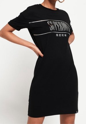 Robe t-shirt noire en coton, présentant un graphique "SUPERDRY" en blanc sur la poitrine. Manches courtes et coupe décontractée.