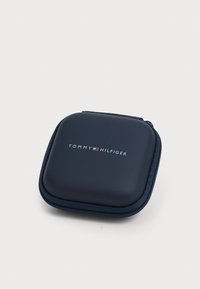 Navy blue hard case with a smooth texture, zip closure, and embossed "TOMMY HILFIGER" logo in white. Square shape with rounded edges.