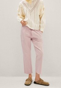 Blusa blanca con rayas verticales y mangas con volantes, combinada con pantalones cortos rosas. El calzado consiste en zuecos sin talón de color beis.