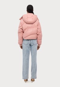 Rosa vadderad jacka med huva, med en boxig form och ribbade manschetter, kombinerad med ljusblå högmidjade jeans.