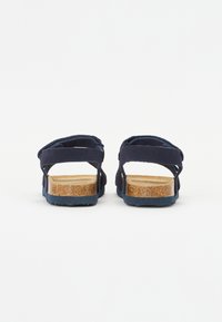 Mörkblå sandaler med två korsade remmar och fotbädd av kork. Gummisula ger bra grepp. Enkel och platt design, lämplig för vardagsbruk.