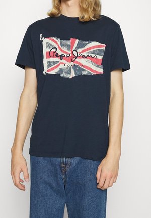 Osoba ubrana w granatowy t-shirt z przetartą flagą Union Jack i napisem „Pepe Jeans London”, do tego niebieskie dżinsy.