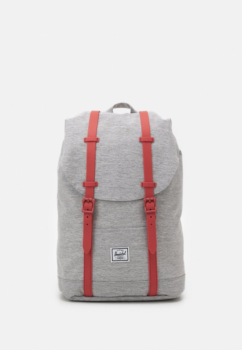 Sac à dos en tissu gris avec des sangles en cuir rouge, rabat arrondi et patch logo sur le devant. Comprend une manche supérieure et des sangles d'épaule réglables.