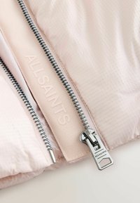 Lichtroze pufferjack met een gestructureerde afwerking, voorzien van een zilveren rits en een reliëflogo langs de sluiting voor extra detail.