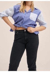 Camisa de rayas azul y blanca con bolsillo en el pecho, diseño corto, con botones en el frente y mangas enrolladas, combinada con jeans negros de tiro alto.
