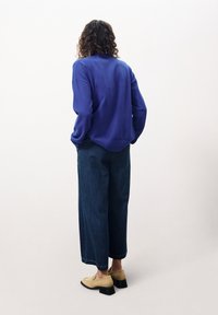 Pull en tricot violet à manches longues, coupe ample et ourlet côtelé. Associé à un jean en denim foncé taille haute et des mocassins beiges.