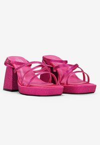 Sandalias de plataforma rosas con tiras cruzadas, textura brillante, adornadas con pedrería en el tacón y la suela, presentando un diseño de tacón cuadrado.