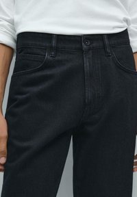 I jeans in denim scuro presentano una vestibilità dritta, un design a cinque tasche, con chiusura a bottone e cuciture a singolo punto. Tessuto strutturato con una finitura liscia.