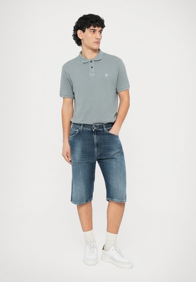 Γκρι κοντομάνικη μπλούζα πόλο με τρία κουμπιά στη λαιμόκοψη, σε συνδυασμό με σκούρο μπλε τζιν σορτς. Το μοντέλο φοράει λευκά αθλητικά παπούτσια και ανοιχτόχρωμες κάλτσες.