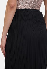 Zwarte plissé rok met een elastische tailleband, voorzien van een sprankelende roségouden pailletten lijfje voor contrast en visuele textuur.