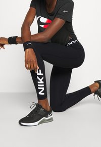 Black athletic leggings with white "NIKE" branding, paired with a black t-shirt featuring a red and white logo, and black athletic shoes.