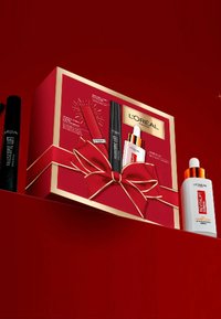 Boîte cadeau L'Oréal avec un extérieur rouge, des accents dorés, ornée d'un nœud. Contient un mascara, un sérum et un correcteur avec des designs d'emballage distincts.
