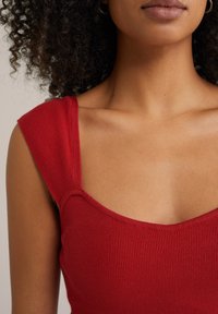 Czerwony, prążkowany top na ramiączkach, z kwadratowym dekoltem i szerokimi ramiączkami. Materiał wydaje się być elastyczny i teksturowany, podkreślając dopasowany krój.
