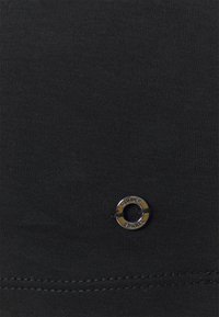 Schwarzer Baumwollstoff mit glatter Textur, der nahe der Unterseite mit einem runden Metallöse beschriftet ist, die "OLIVER" lautet.