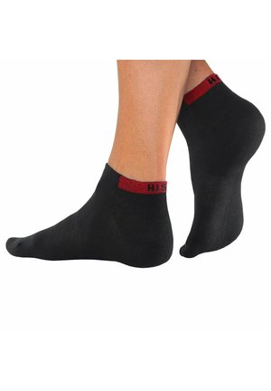 Black ankle socks with a red knitted band at the top, displaying the text "HIS." The fabric appears smooth and elastic in texture.