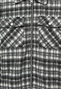 Giacca in flanella grigia e bianca a quadri con cerniera frontale, due tasche sul petto con patte con bottoni e un aspetto morbido e strutturato.