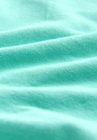 Un tissu bleu clair au toucher doux, avec une texture subtile et des plis. Le matériau semble lisse et légèrement extensible, offrant une esthétique épurée.