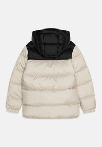 Doudoune avec une capuche noire rembourrée et un corps beige. Présente une texture matelassée, des poignets élastiques et une finition lisse.