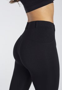 Czarne legginsy o wysokim stanem, gładkiej fakturze i dopasowanym kroju, z średniej wysokości pasem i bez widocznych logo.