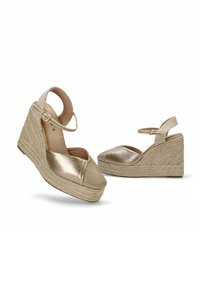Sandalias de cuña con un upper metálico dorado y una puntera de tela beige, que cuentan con una plataforma de yute trenzado y una correa para el tobillo con hebilla ajustable.