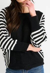 Maglione a righe bianche e nere con polsini a coste e un corpo texturizzato, caratterizzato da ampie righe inclinate sulle maniche su uno sfondo solido.