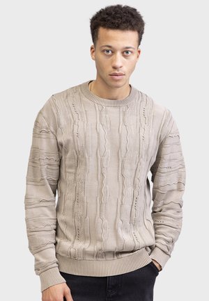 Maglione beige chiaro con texture, caratterizzato da motivi in rilievo e polsini a coste. Il design include linee orizzontali e dettagli di cucitura vari.