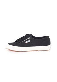 Sorte kanvas sneakers med hvit gummisåle, snøring, og en liten merke logo detalj nær snøringene. Strukturert overflate.