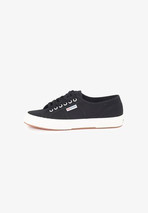 Sneaker nera in tela con suola in gomma bianca, design con lacci e piccolo logo del marchio vicino ai lacci. Superficie testurizzata.
