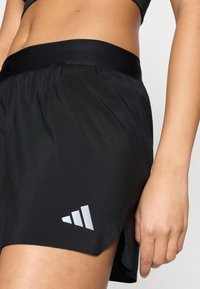 Pantalones cortos deportivos negros con una textura suave, que cuentan con una cinturilla elástica ancha y un detalle de logo plateado en el lateral.