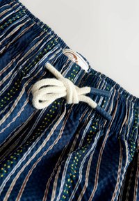 Close-up of navy blue striped shorts with yellow star accents, elastic waistband, and white drawstring tied in a bow with "NEXT" branded tips.