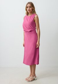 Rosa ärmelloses Kleid aus glattem Stoff, mit einem taillierten Oberteil und einem fließenden Midi-Rock; getragen mit weißen Riemchensandalen.