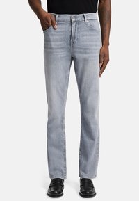 Jeans grigio chiaro in denim sbiadito con taglio dritto, design a cinque tasche e chiusura con bottone in metallo. Indossati con scarpe nere.