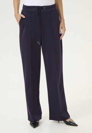 Purple wide-leg pants with a drawstring waist, side pockets, and a smooth texture, paired with black pointed-toe heels.